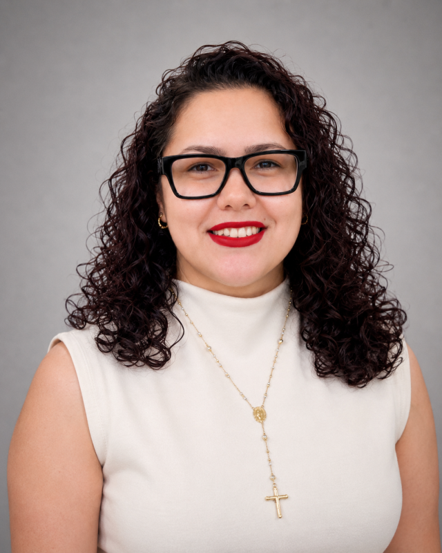 Portrait of Katia, dental team member with curly hair and glasses smiling at the camera